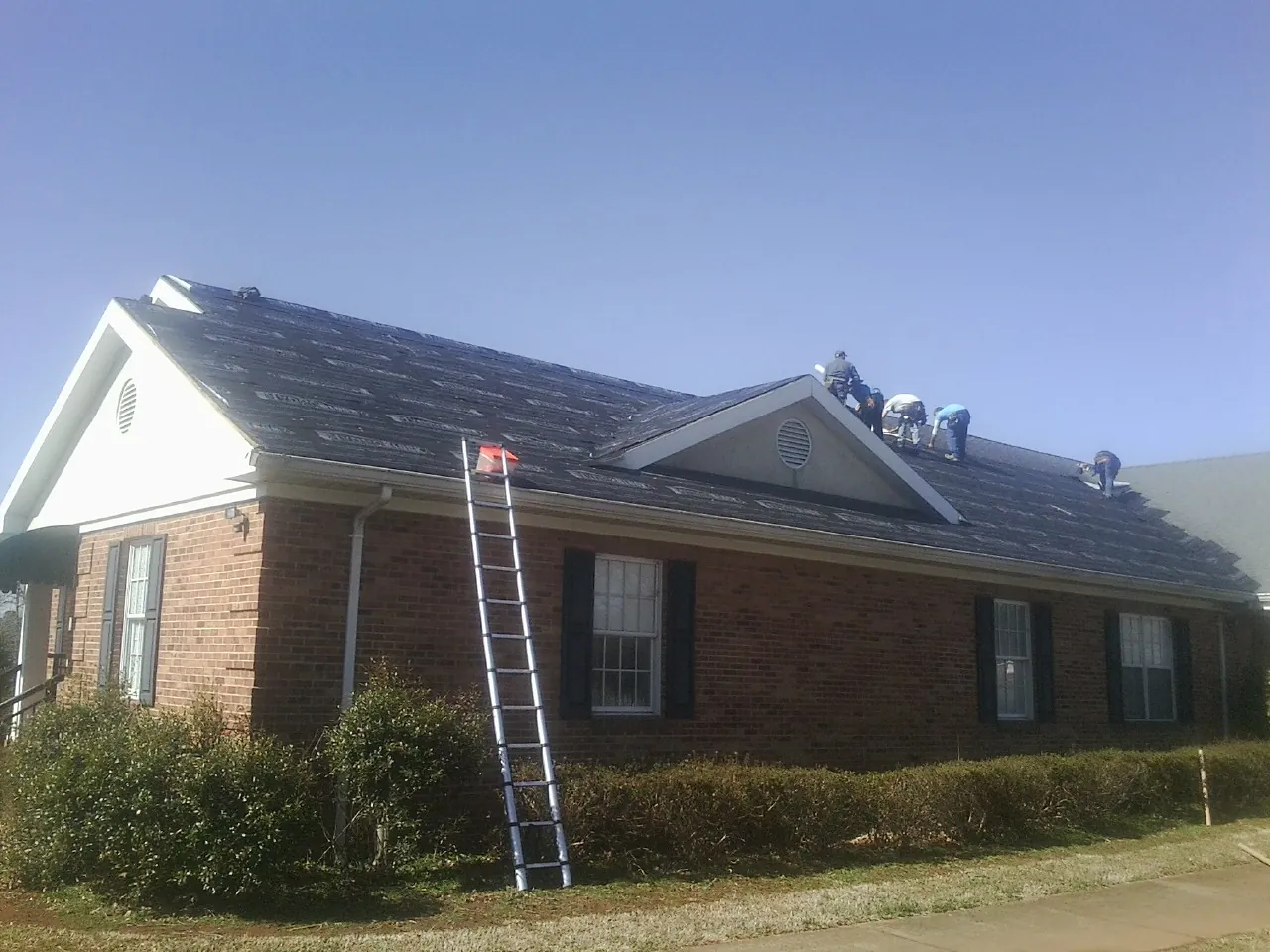 Crew tearing shingles off a brick ranch roof with a ladder set — Emergency Roof Repair work by our crew in Albertson