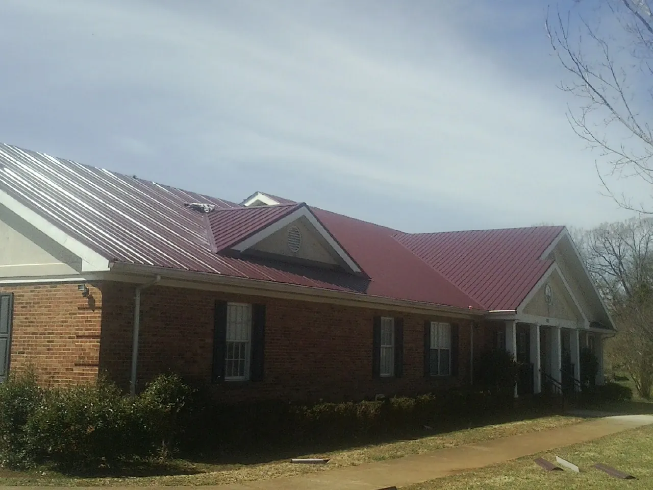 Red metal roof with gabled entries on a long brick building, from a Hail Damage Roof Repair job in Albertson