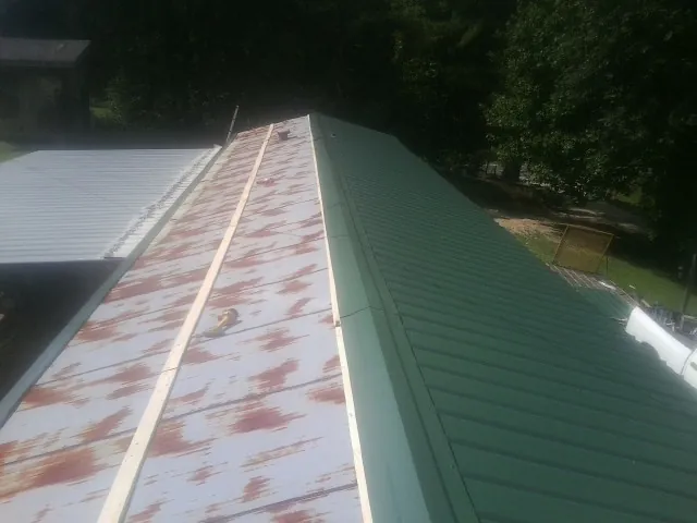 Old rusted panels beside newly installed green metal roofing — Wind Damage Roof Repair by Roofing Brothers in Albertson