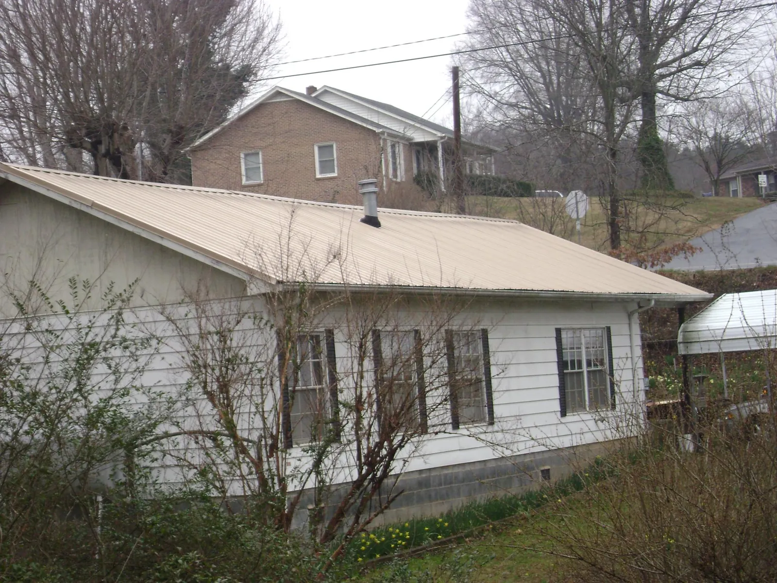 Tan metal roof on a white sided house set into a hillside — Commercial Roofing by Roofing Brothers in Albertson