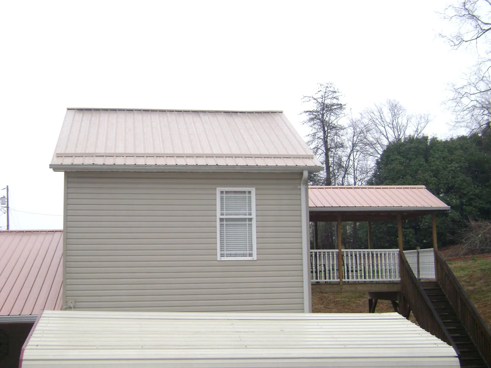 Tan metal roofs on a two story addition and attached porch, from a Roof Replacement job in Albertson